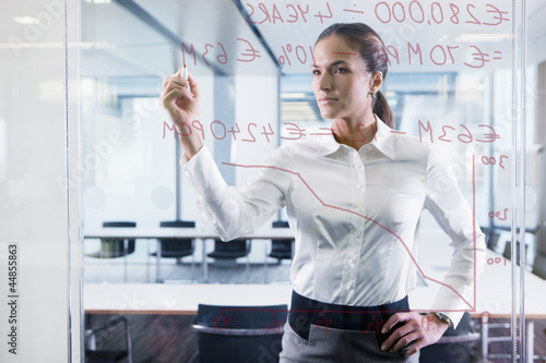 Photo: Businesswoman drawing graph on glass window in office Businesswoman drawing graph on glass window in office