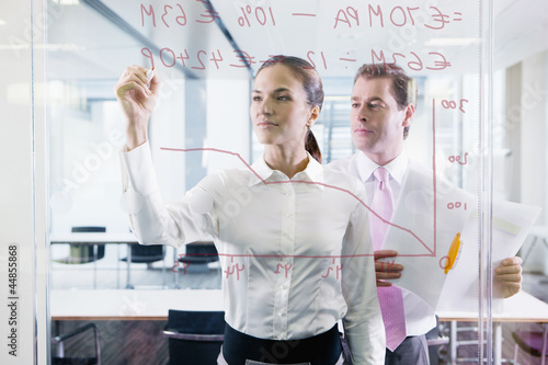 Photo: Businessman and businesswoman drawing chart on glass window in office Businessman and businesswoman drawing chart on glass window in office