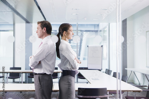 Photo: Businessman and businesswoman standing back to back in conference room Businessman and businesswoman standing back to back in conference room