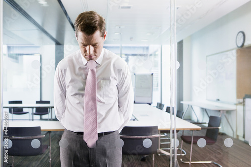 Photo: Dejected businessman leaning on glass window in conference room Dejected businessman leaning on glass window in conference room
