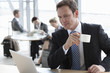 Smiling businessman drinking coffee and using laptop
