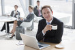 Portrait of smiling businessman drinking coffee and using laptop