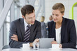 Businessman and businesswoman using digital tablet at table in lobby