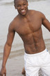 Photo: Portrait of smiling, wet bare chested young man kneeling on beach Portrait of smiling, wet bare chested young man kneeling on beach