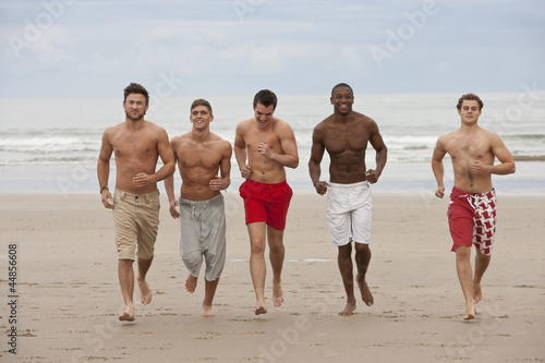 Photo: Smiling young men running bare chested on beach Smiling young men running bare chested on beach