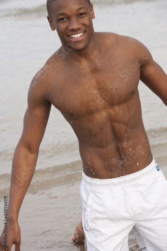 Photo: Portrait of smiling, wet bare chested young man kneeling on beach Portrait of smiling, wet bare chested young man kneeling on beach