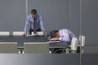 Photo: Businessman reading paperwork near co-worker sleeping on laptop in conference room Businessman reading paperwork near co-worker sleeping on laptop in conference room