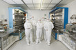 Photo: Portrait of scientists in clean suits standing in silicon wafer manufacturing laboratory Portrait of scientists in clean suits standing in silicon wafer manufacturing laboratory