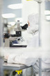 Photo: Scientist in clean suit examining silicon wafer under microscope in clean room laboratory Scientist in clean suit examining silicon wafer under microscope in clean room laboratory