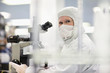 Foto: Portrait of scientist in clean suit examining silicon wafer under microscope in clean room laboratory Portrait of scientist in clean suit examining silicon wafer under microscope in clean room laboratory