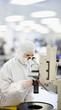 Photo: Scientist in clean suit examining silicon wafer under microscope in clean room laboratory Scientist in clean suit examining silicon wafer under microscope in clean room laboratory
