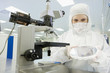 Photo: Scientist in clean suit examining silicon wafer next to microscope in laboratory Scientist in clean suit examining silicon wafer next to microscope in laboratory