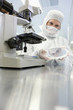 Photo: Scientist in clean suit examining silicon wafer next to microscope in laboratory Scientist in clean suit examining silicon wafer next to microscope in laboratory