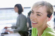 Close up of smiling businesswoman wearing headset in office with co-worker in background