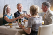 Happy, well-dressed couples toasting wine glasses at restaurant table