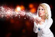 junge blonde Frau im Winteroutfit pustet Schnee