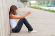 Sad teenage girl sitting alone in urban environment