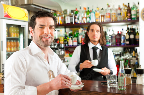 Photo: Barista with client in his cafe or coffeeshop Barista with client in his cafe or coffeeshop