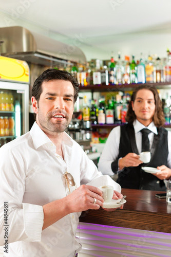 Photo: Barista with client in his cafe or coffeeshop Barista with client in his cafe or coffeeshop