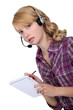A businesswoman with a headset on taking notes.
