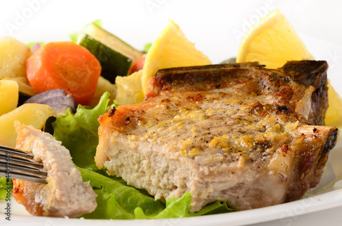 Photo: Roasted pork chop garnished with vegetables on white Roasted pork chop garnished with vegetables on white