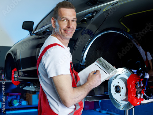Photo: Car mechanic in a garage looking at repair costs for a bracke Car mechanic in a garage looking at repair costs for a bracke