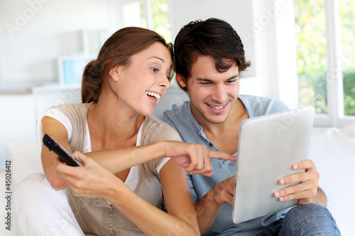 Photo: Cheerful couple choosing tv program on digital tablet Cheerful couple choosing tv program on digital tablet