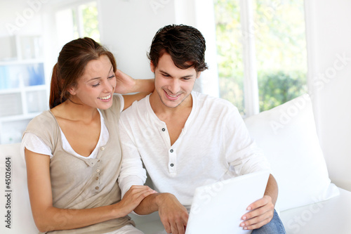 Photo: Happy young couple using laptop computer at home Happy young couple using laptop computer at home