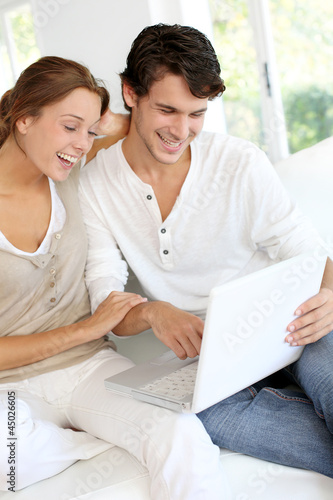Photo: Happy young couple using laptop computer at home Happy young couple using laptop computer at home