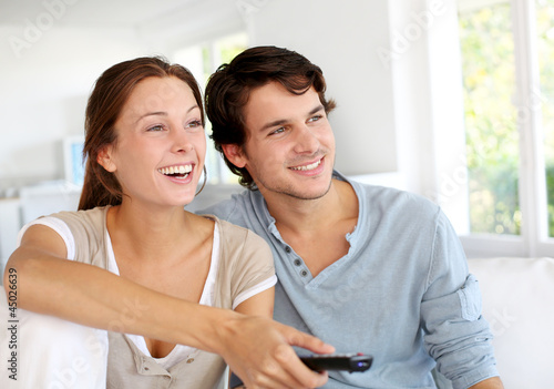 Photo: Couple sitting in sofa with remote control in hands Couple sitting in sofa with remote control in hands