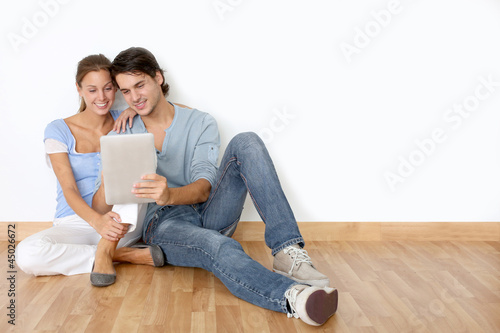 Photo: Couple using tablet laying on the floor at home Couple using tablet laying on the floor at home