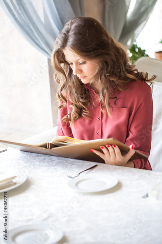 Photo: A woman in a restaurant with the menu in hands A woman in a restaurant with the menu in hands