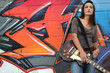 Woman with guitar in front of graffiti
