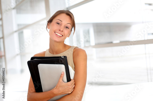 Photo: Smiling businesswoman holding documents in hall Smiling businesswoman holding documents in hall