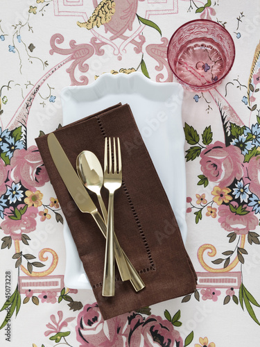 Photo: Plate with napkin and cutlery on floral tablecloth Plate with napkin and cutlery on floral tablecloth