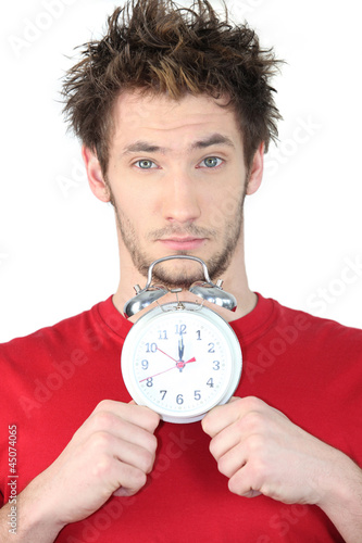 Photo: young guy with swollen eyes showing alarm clock young guy with swollen eyes showing alarm clock