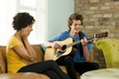 "USA, Utah, Provo, young man playing guitar with young woman covering ears"