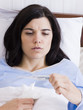 "Orem, Utah, USA, young ill woman in bed looking at thermometer."