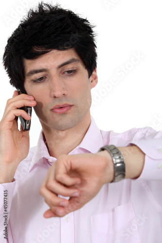 Photo: A businessman over the phone looking at his watch. A businessman over the phone looking at his watch.