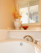 White tub with vase and window corner with beige wall.