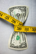 Studio shot of yellow measure tape squeezing two one dollar bills
