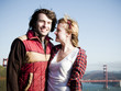 Photo: "USA, California, San Francisco, young couple standing, Golden Gate Bridge in background" "USA, California, San Francisco, young couple standing, Golden Gate Bridge in background"