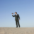 "USA, Utah, Little Sahara, businessman looking through telescope in desert"