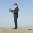 "USA, Utah, Little Sahara, businessman looking through telescope in desert"
