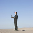 "USA, Utah, Little Sahara, businessman looking through telescope in desert"