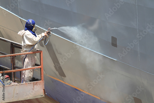 Photo: worker painting ship hull using airbrush gray paint worker painting ship hull using airbrush gray paint
