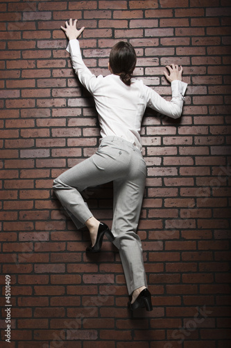 Photo: Studio shot of young woman climbing up brick wall Studio shot of young woman climbing up brick wall