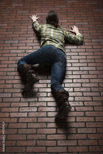 Photo: Studio shot of young woman climbing up brick wall Studio shot of young woman climbing up brick wall