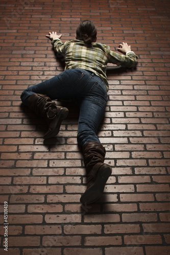 Photo: Studio shot of young woman climbing up brick wall Studio shot of young woman climbing up brick wall