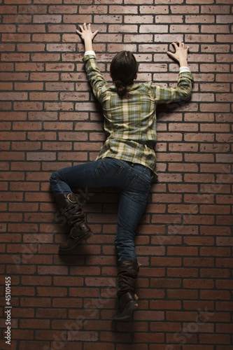 Photo: Studio shot of young woman climbing up brick wall Studio shot of young woman climbing up brick wall
